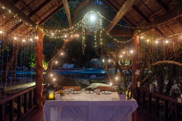 Obraz premium Romantic dinner setup with fairy lights in outdoor wooden gazebo at night