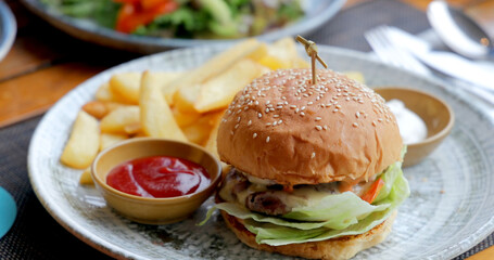 Juicy cheeseburger with lettuce and tomato served with crispy fries and ketchup on rustic table. Fresh fast food meal in casual dining setting.