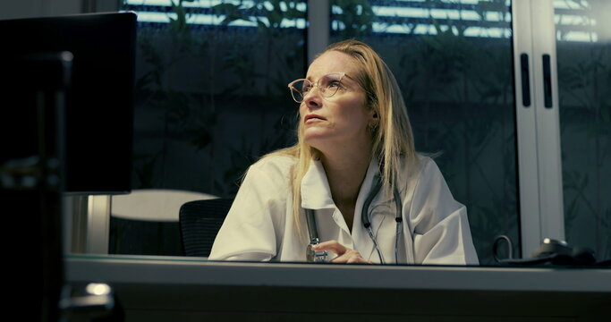 Female doctor in distress during night shift, facing intense emotional pressure while sitting at desk in clinical setting, struggling with overwhelming workload