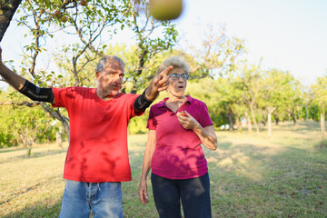 Elderly son and his mother standing under apple tree, enjoying the outdoor environment on their sunny day.