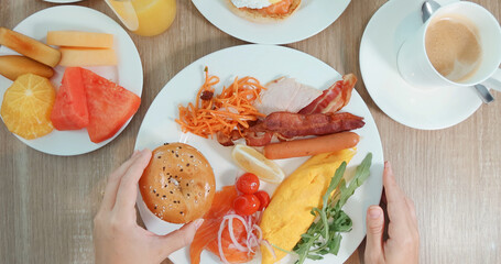 Breakfast plate with omelette, bacon, sausage, smoked salmon, mixed fruit on wooden table. Hands ready to eat. Fresh, healthy, balanced meal concept.