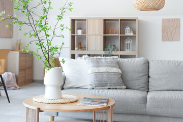 Interior of stylish living room with cozy sofa, coffee table and blooming tree branches in vase