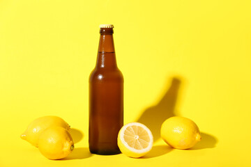 Bottle of fresh beer with lemons on yellow background