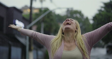 Woman raising arms and looking upward in rain, overwhelmed with joy, gratitude, and emotional...