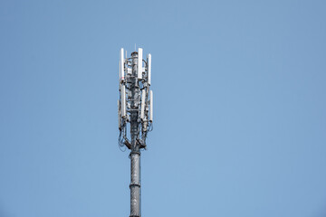 A cellular communication tower with 5G and 4G antennas against a clear blue sky. Technology and telecommunication network infrastructure concept.