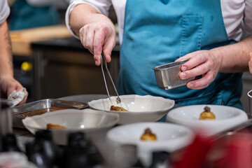 Main d’un chef étoilé en pleine préparation culinaire, dressant un plat gastronomique avec précision.