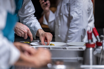 Main d’un chef étoilé en pleine préparation culinaire, dressant un plat gastronomique avec précision.