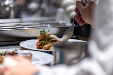 Main d’un chef étoilé en pleine préparation culinaire, dressant un plat gastronomique avec précision.