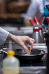 Mains d’un chef en train de faire cuire des langoustines dans une poêle chaude en cuisine professionnelle.