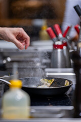 Mains d’un chef en train de faire cuire des langoustines dans une poêle chaude en cuisine professionnelle.