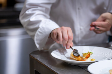 Mains d’un chef étoilé en train de préparer un plat gastronomique, déposant du caviar de Madagascar sur une langoustine.
