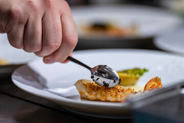 Mains d’un chef étoilé en train de préparer un plat gastronomique, déposant du caviar de Madagascar sur une langoustine.