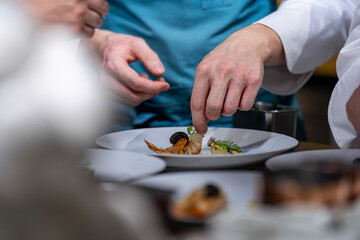 Main d’un chef étoilé en pleine préparation culinaire, dressant un plat gastronomique avec précision.