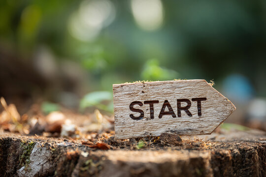 Wooden arrow sign in nature says Start new beginning journey adventure path way forest woods