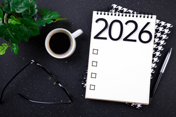 Naklejka premium New year resolutions 2026 on desk. 2026 goals list with notebook, coffee cup, plant on black table. Resolutions, plan, goals, action, checklist, idea concept. New Year 2026 resolutions, copy space