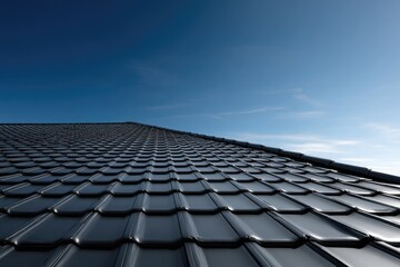 Perspective view of a dark, tiled roof against a clear, blue sky