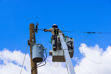 Electrical utility worker uses cherry picker to repair electrical lines on pole under work...