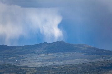Mountain landscape under dramatic sky with rain clouds sweeping across the horizon