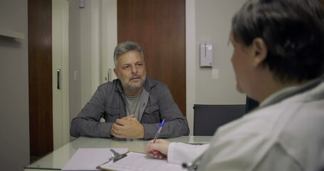 Obraz premium Close-up of middle-aged man patient in discussion with doctor during medical consultation at desk with clipboard and notes