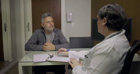 Obraz premium Close-up of middle-aged man patient in discussion with doctor during medical consultation at desk with clipboard and notes