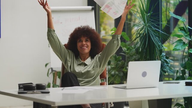 Excited African American businesswoman throwing papers in air, celebrating win