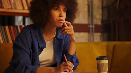 Thoughtful black female journalist making a draft for an article in city library