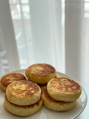 Golden cottage cheese pancakes syrniki on a white plate near the window