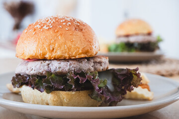 Close-up of a delicious burger with sesame seed bun, savory patty, and fresh red leaf lettuce on a plate, an inviting healthy meal concept.
