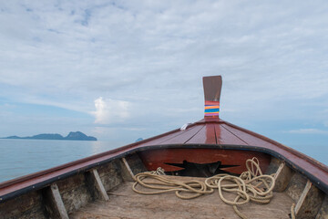 View from the bow of a traditional longtail boat on calm water, with distant islands under a cloudy sky, evoking tropical travel and adventure.