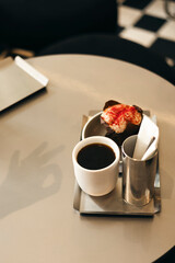 Cup of black coffee and muffin with white icing and red sprinkles on a table.