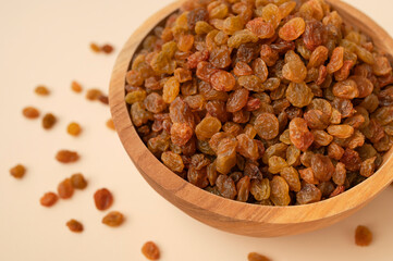 Sweet brown golden raisins in wooden bowl on beige background flat lay top view. Dried grapes berries. Food background. Ingredient for cooking, baking desserts