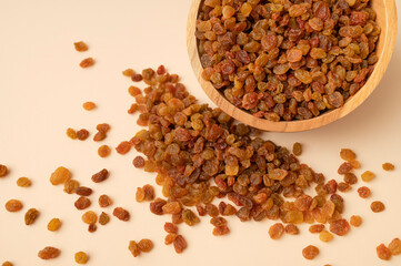Sweet brown golden raisins in wooden bowl on beige background flat lay top view. Dried grapes berries. Food background. Ingredient for cooking, baking desserts