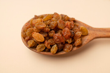 Dried golden brown raisins in wooden spoon on beige background flat lay top view. Grapes berries, sweet healthy snack, organic dried fruits. Food background

