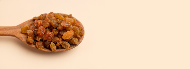 Dried golden brown raisins in wooden spoon on beige background flat lay top view. Grapes berries, sweet healthy snack, organic dried fruits. Food background
