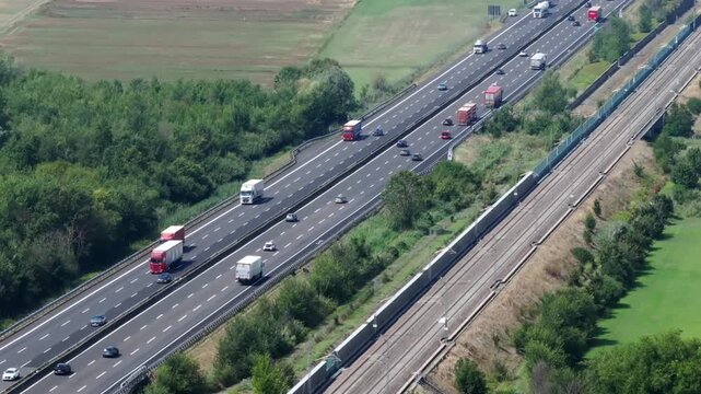 Aerial view of busy Italian highway A1 with trucks and cars traveling on a sunny day. Traffic flows along the Autostrada del Sole, a major Italian transport artery, showcasing the movement of goods
