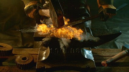 The blacksmith manually forging the molten metal on the anvil in smithy with spark fireworks