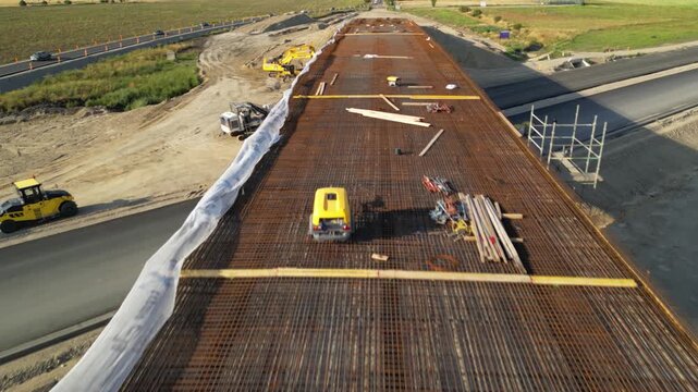 Top-down aerial view of a construction foundation covered with a dense steel reinforcement mesh, with timber formwork, tools and building materials prepared before concrete pouring.