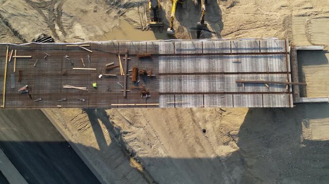 Top-down aerial view of a construction foundation covered with a dense steel reinforcement mesh, with timber formwork, tools and building materials prepared before concrete pouring.
