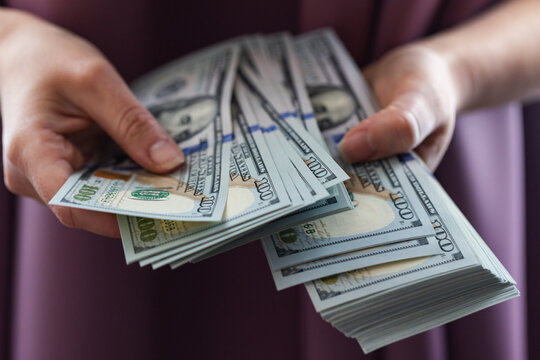 A person's hands holding and counting a stack of one hundred dollar bills.