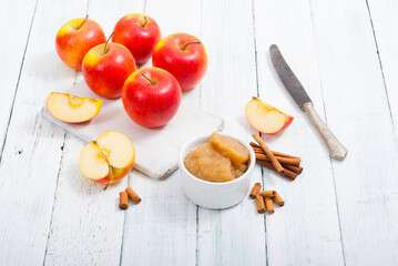 apple jam at porcelain dish, apples, cinnamon, white wood table background