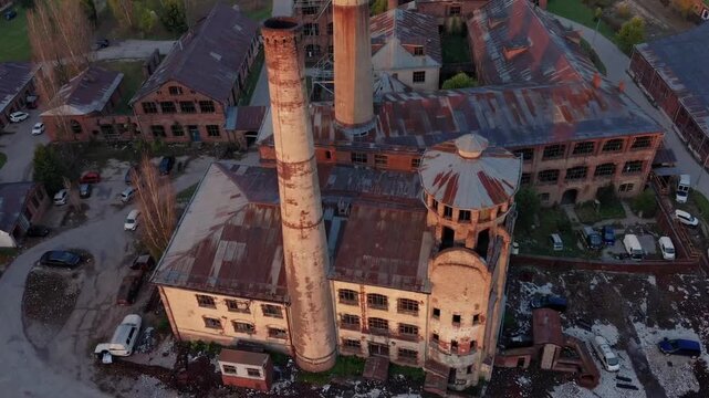 dated deserted manufacturing plant featuring elevated smoke conduits positioned in pastoral setting near hamlet enveloped by emerald pastures and undulating elevations