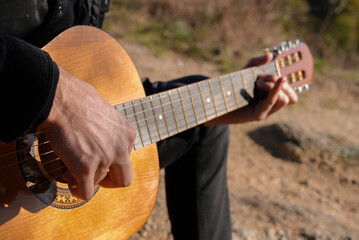 Close up hands of artist plays wooden acoustic guitar in autumnal park. Young songwriter plays string musical instrument hobby outside in nature fall time. Audio music healing in natural surrounding. 
