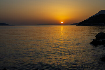 Sunset behind the mountain at the Adriatic Sea with reflection on the water. Podaca village, Makarska Riviera, South Dalmatia, Croatia.
