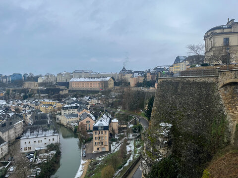 View of the cliffs beside the Alzette River in Grund on a winter day with snow and cloudy skies. Luxembourg