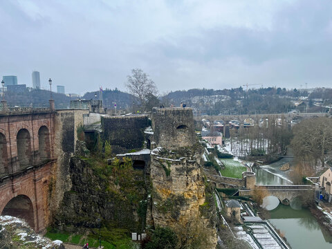 View of the cliffs beside the Alzette River in Grund on a winter day with snow and cloudy skies. Luxembourg