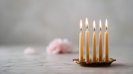 Five candles lit in elegant holder with pink flowers in background  