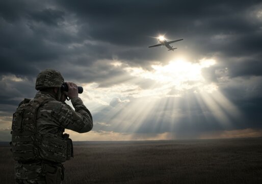 Soldier using binoculars to observe military drone flying in dramatic cloudy sky with sun rays shining through clouds.