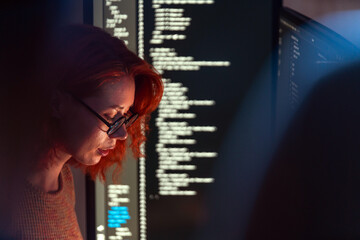 Focused programmer and software developer works in dark workspace, screen glowing with code. Scene highlights programming, coding, technology, data, engineering, and cybersecurity expertise.