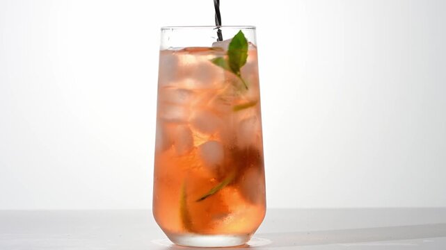 lemonade being stirred in a glass with ice, lemon, and mint on a white background