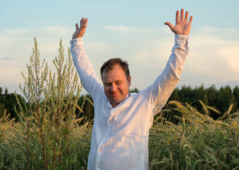 Man in a white shirt standing in a ripe rye field with arms raised, smiling under warm sunlight during golden hour. The scene conveys joy, freedom, and connection to nature